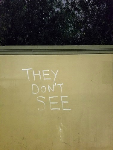 words "they don't see" spray painted in white on a wall along Selma Avenue